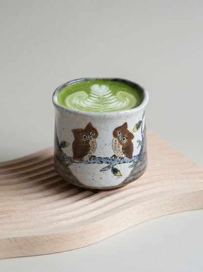 Ceramic cup with owl design filled with green matcha on a wooden surface.