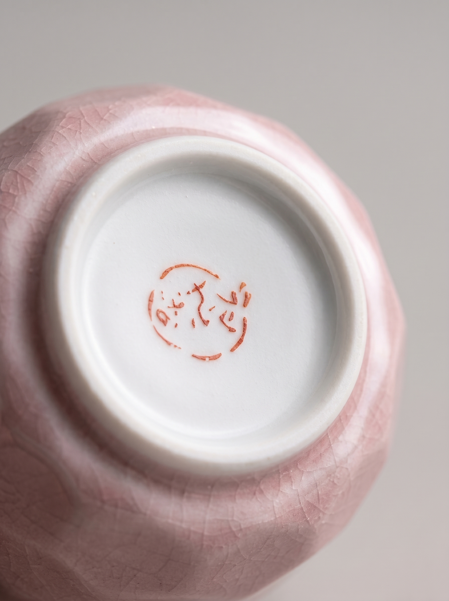 Close-up of a pink ceramic cup with a white interior and red stamp on the bottom.