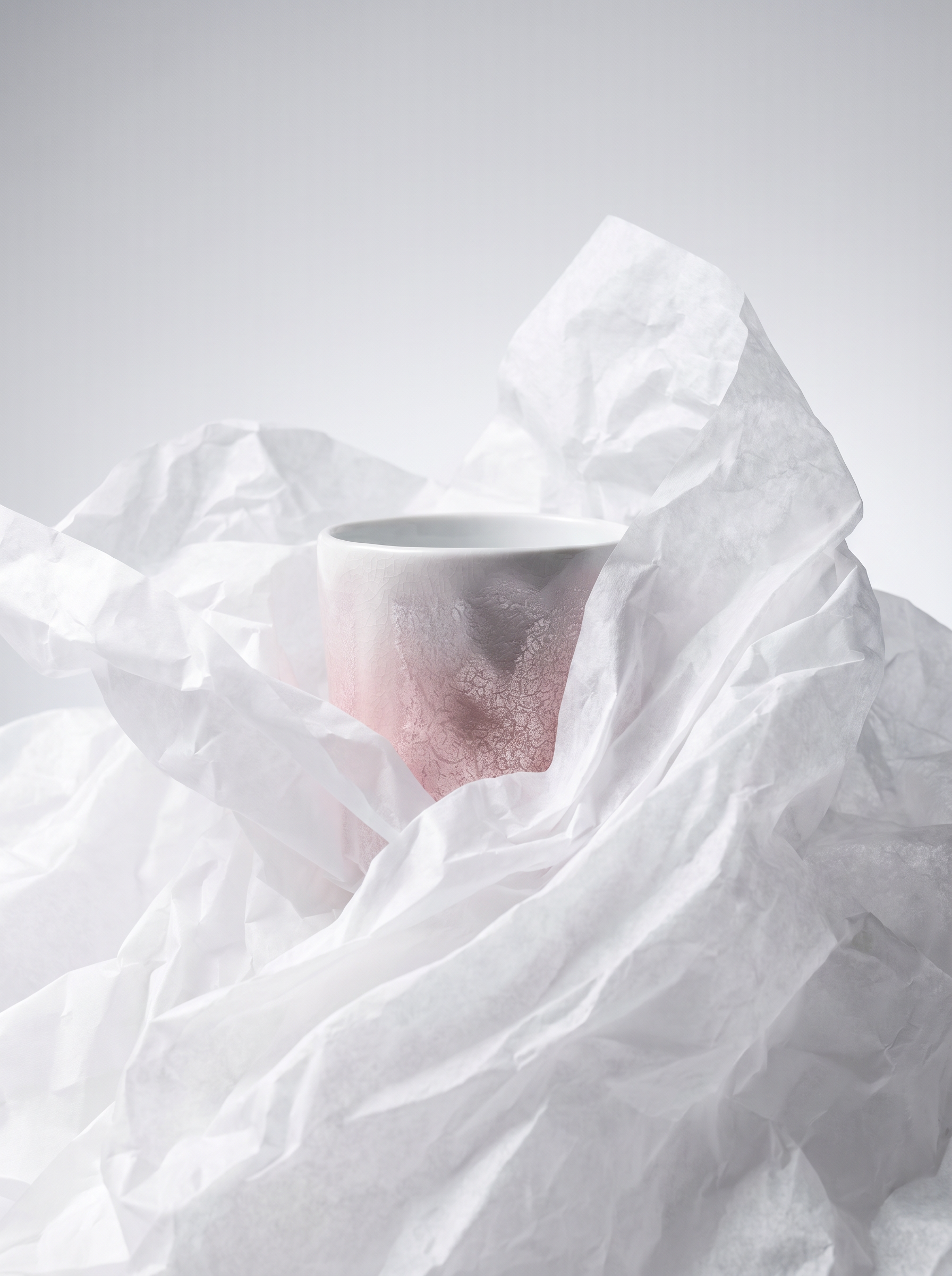 White ceramic cup partially covered by crumpled white paper on a light gray background