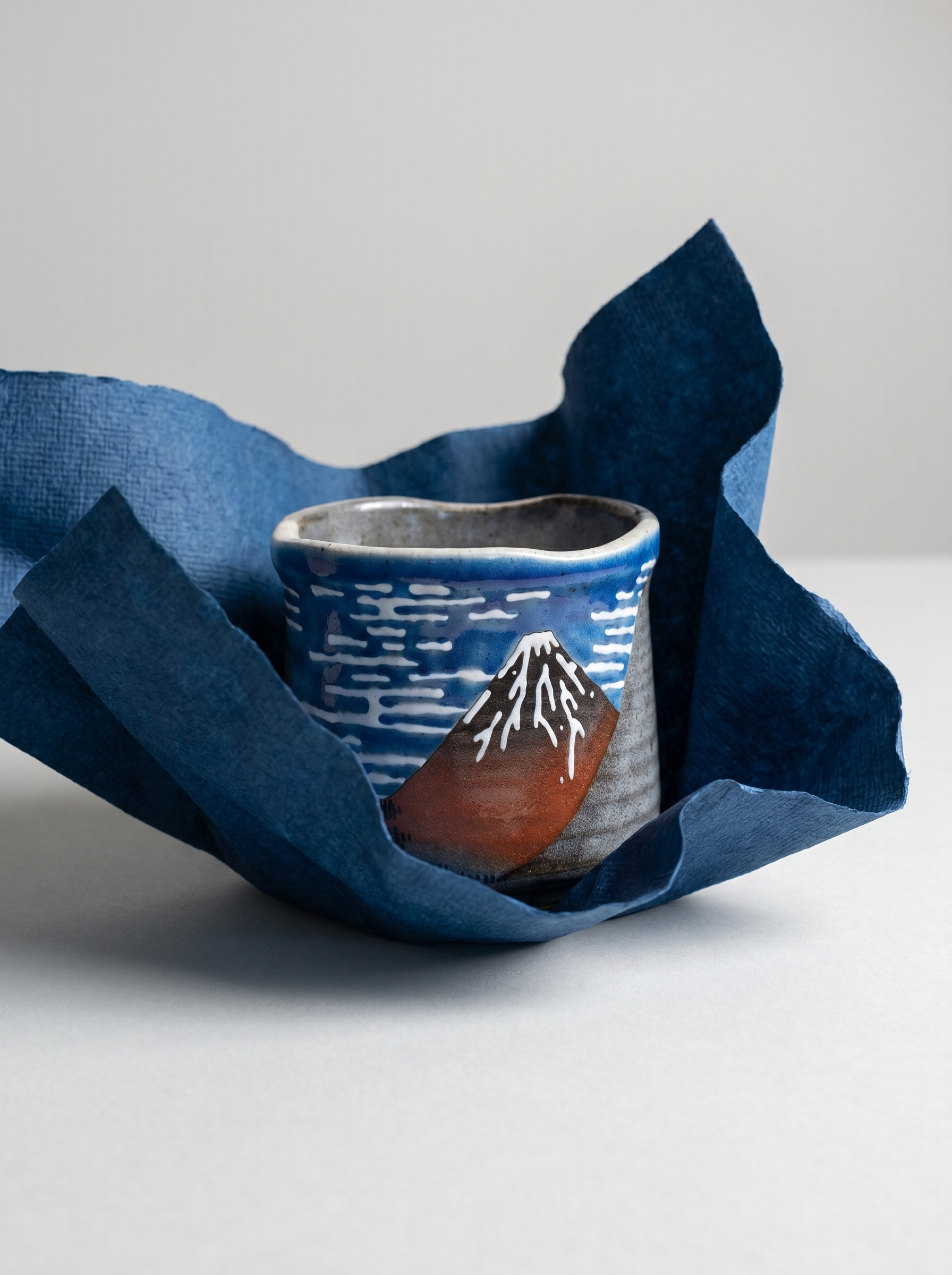Ceramic cup with mountain design wrapped in blue fabric on a light gray background