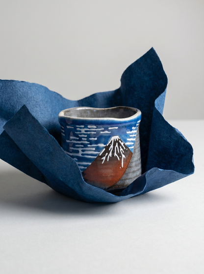 Ceramic cup with mountain design wrapped in blue fabric on a light gray background