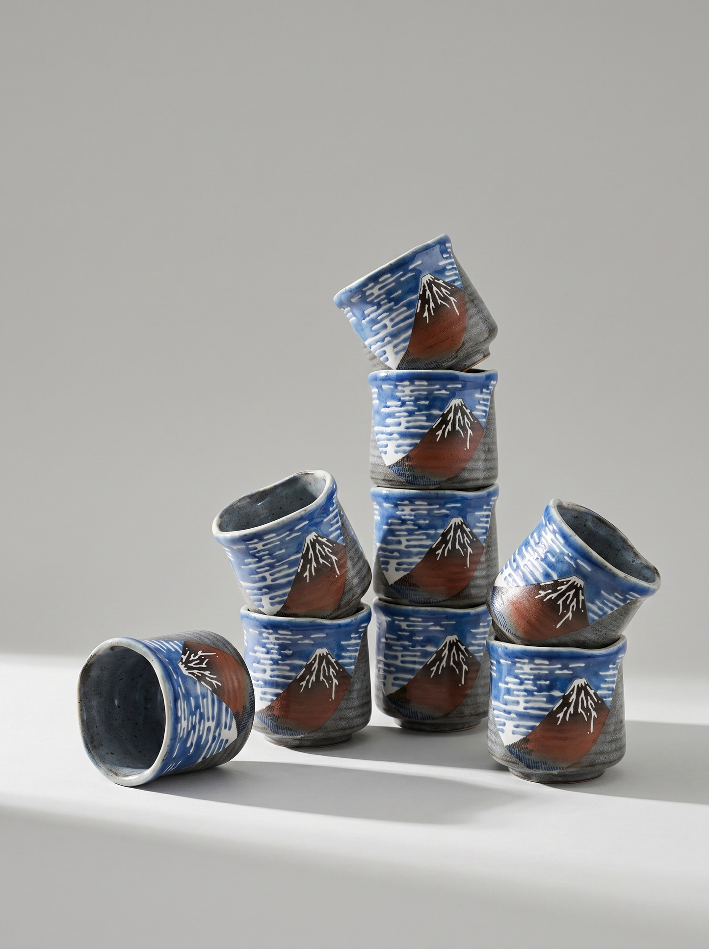 Stack of ceramic cups with Fuji mountain design on a gray background