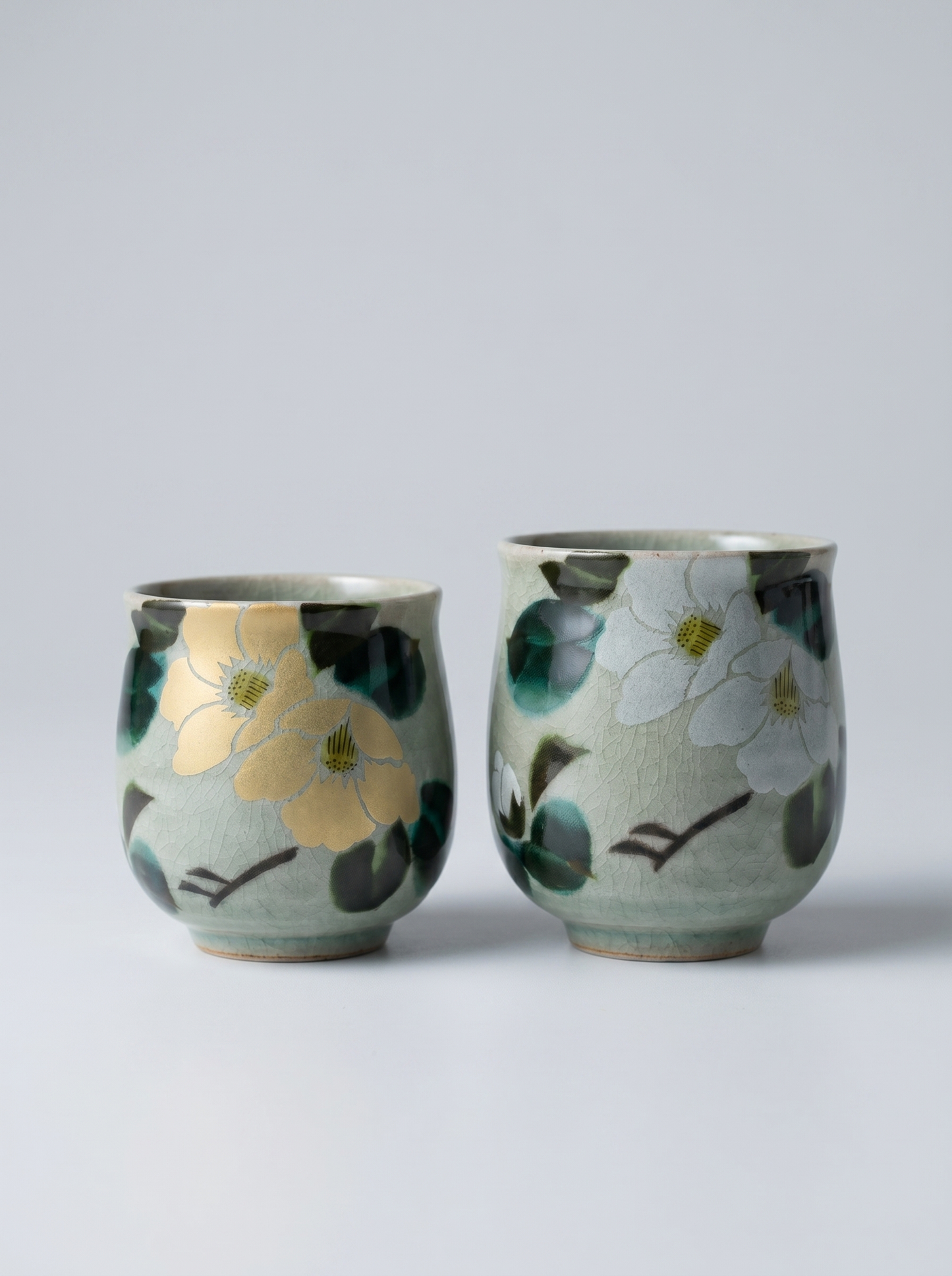Two Japanese ceramic cups with floral designs on a light gray background