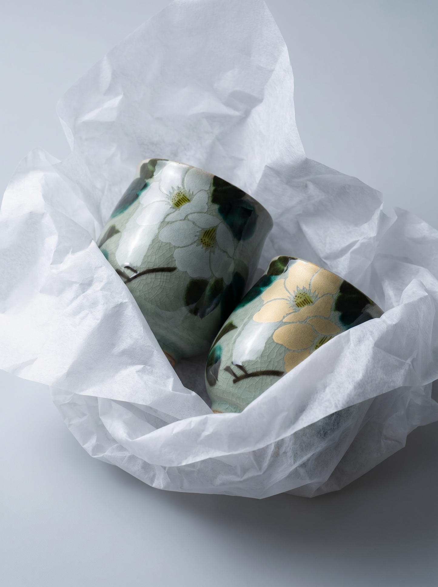 Two ceramic containers with floral designs on a white background covered with white paper tissue