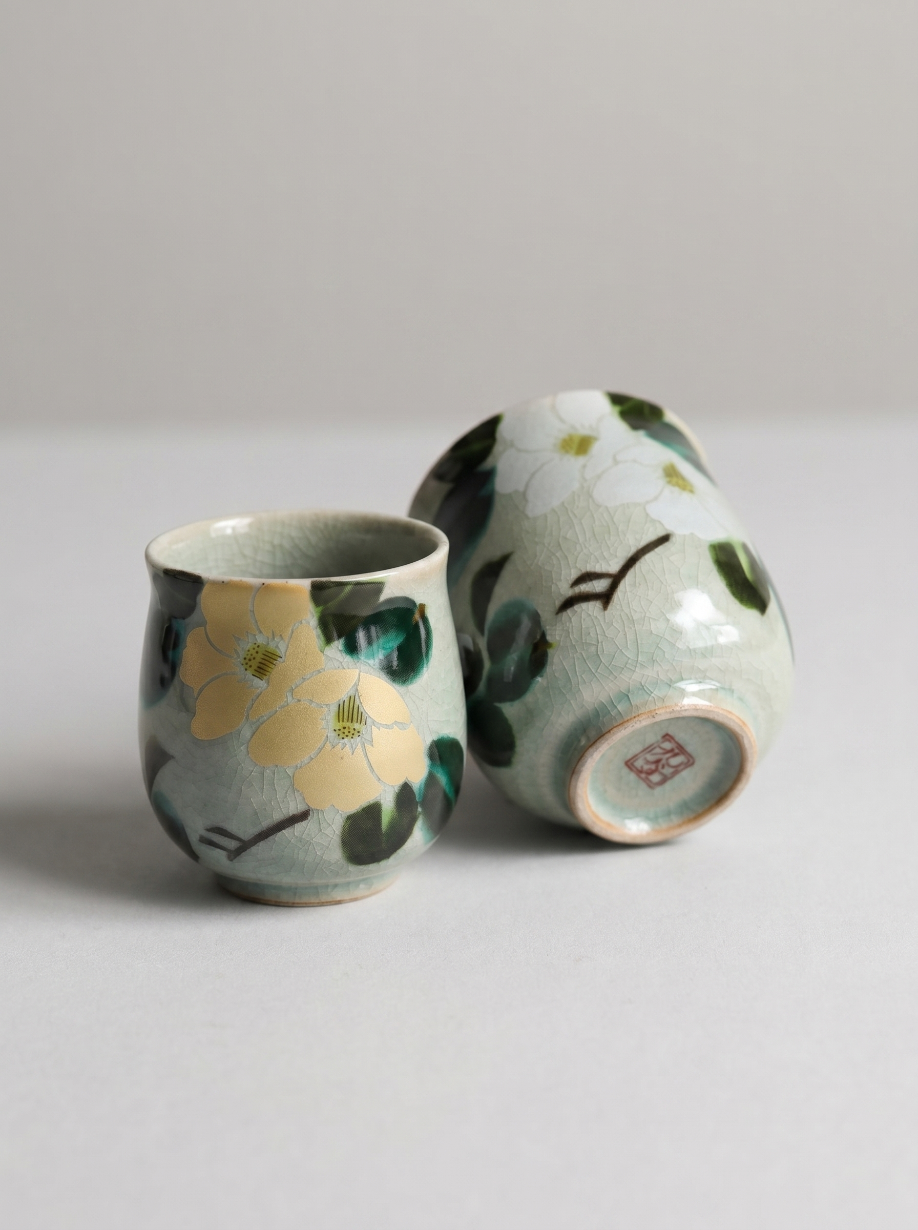 Two ceramic cups with floral designs on a light gray background side view