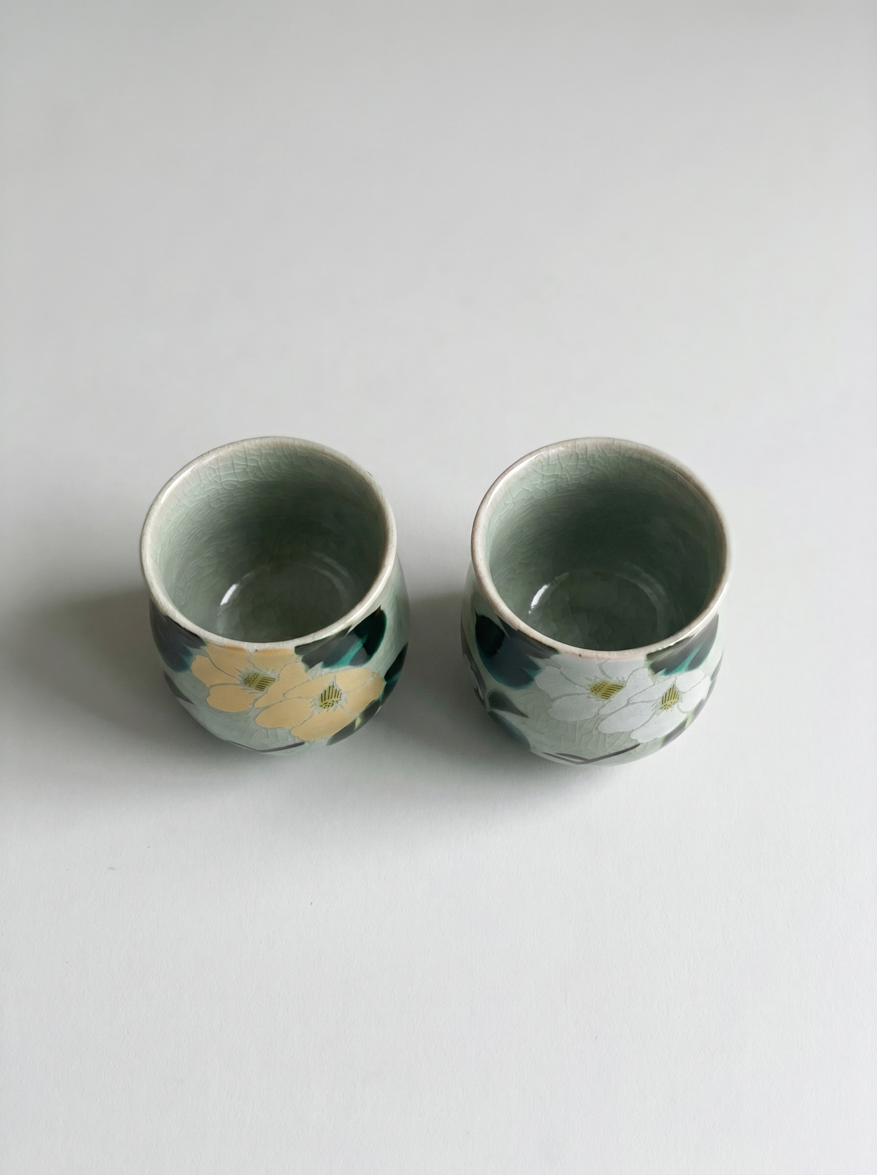 Two ceramic cups with floral patterns on a light gray background