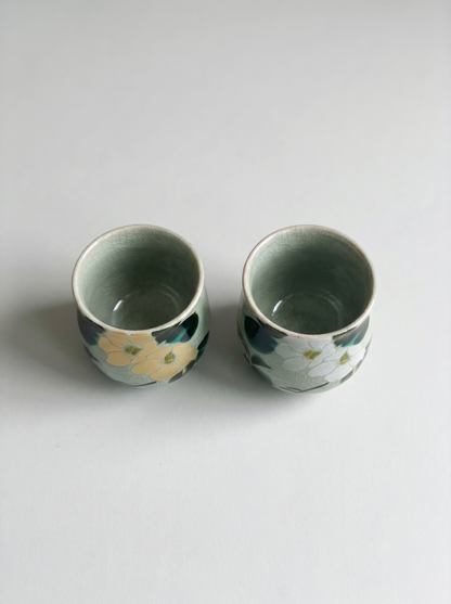 Two ceramic cups with floral patterns on a light gray background