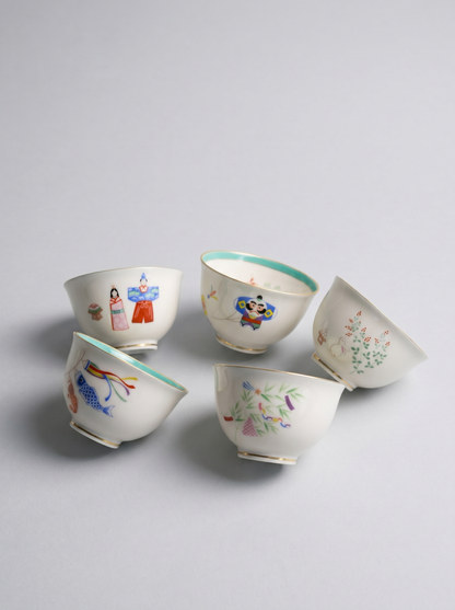 Five ceramic cups with colorful illustrations on a light gray background