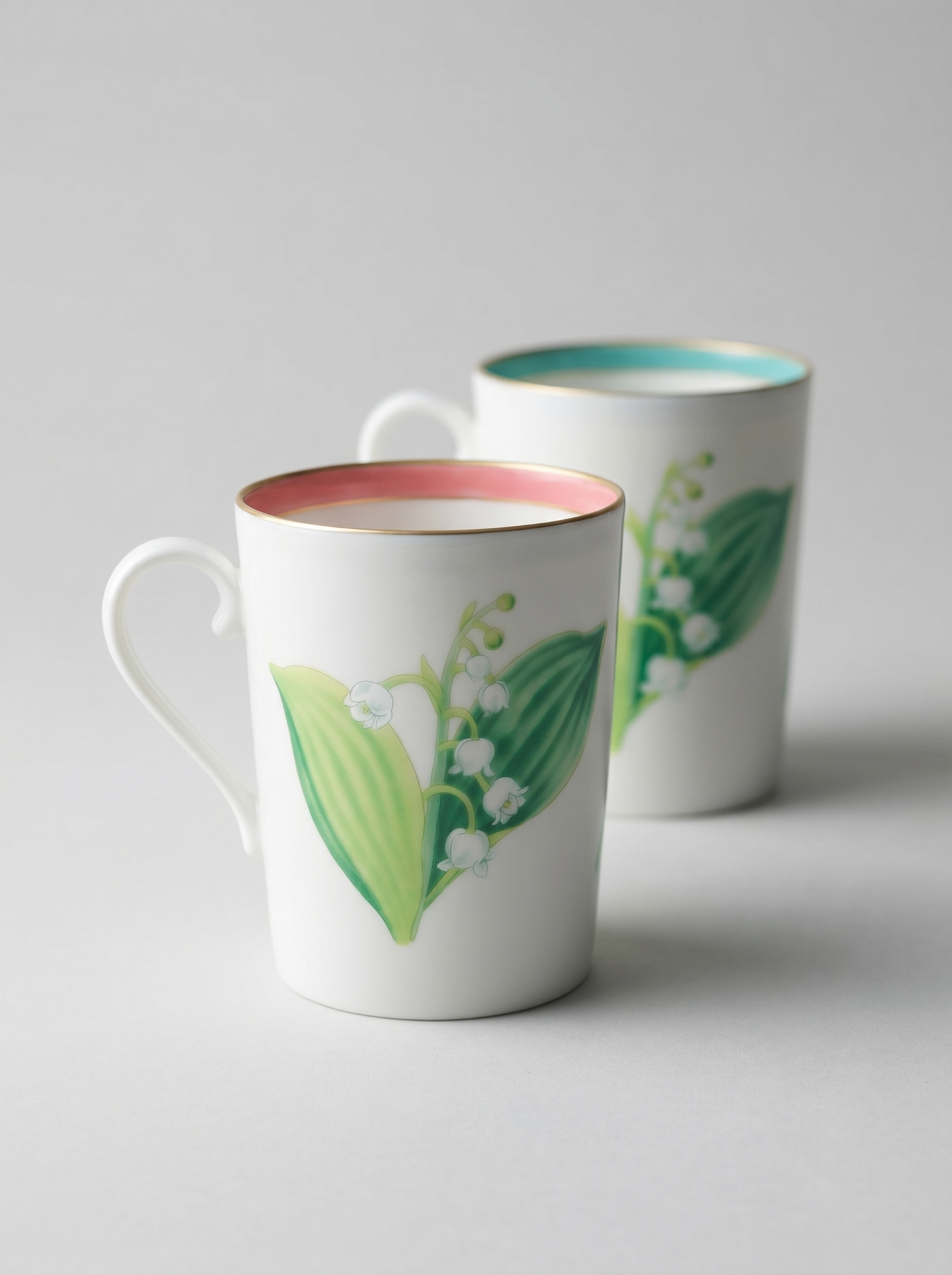 Japanese koransha porcelain set of 2 teacups with short handles and a lily of the valley design in turquoise and coral colors, blurred background