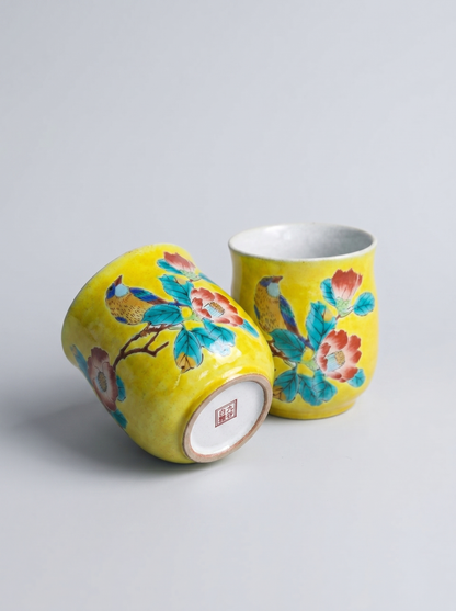 Two yellow ceramic cups with floral designs on a light gray background