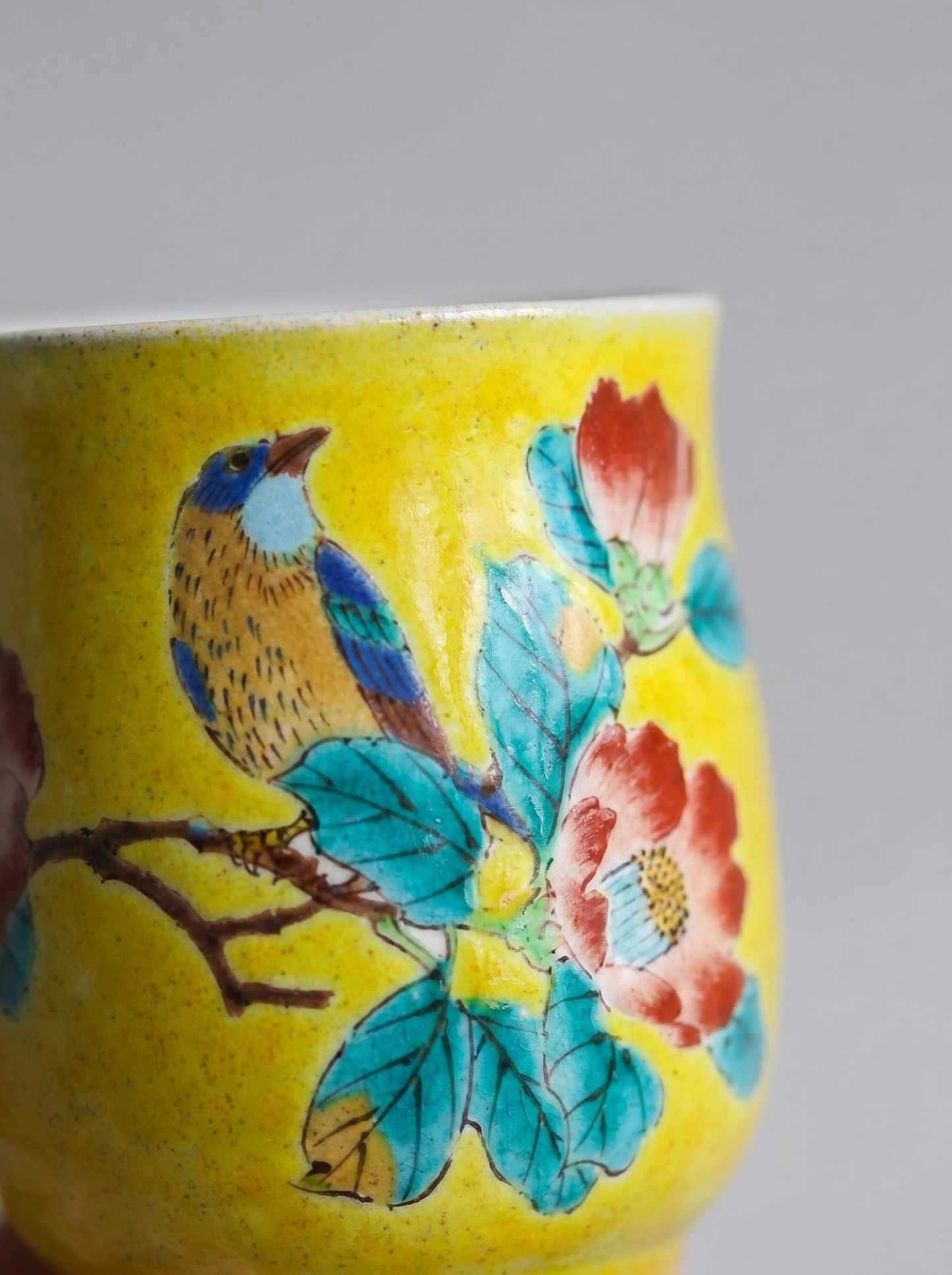 Close up of yellow Japanese ceramic teacup with colorful bird and floral design on a plain background