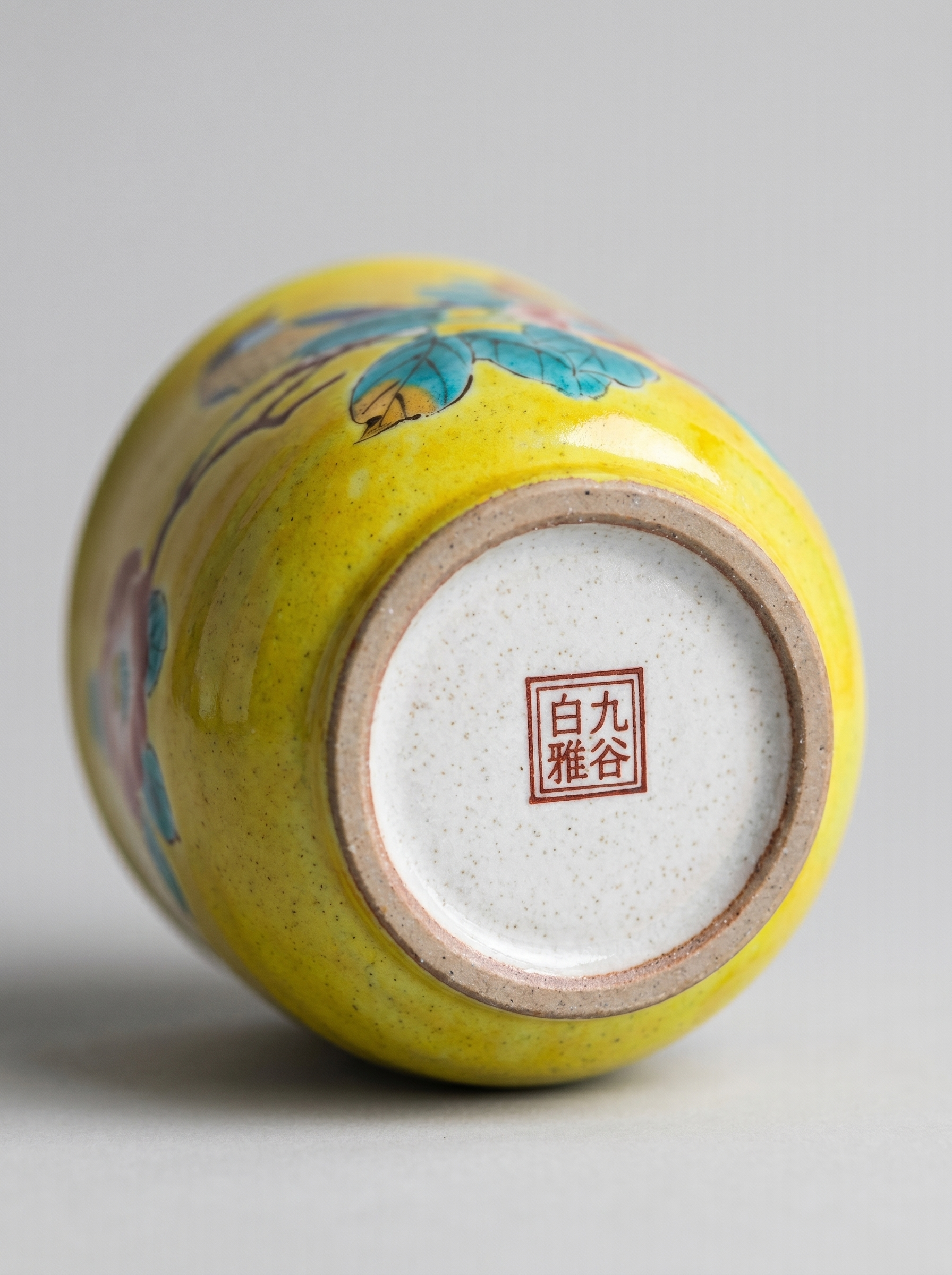 Yellow ceramic cup with floral design and Japanese stamp on a gray background