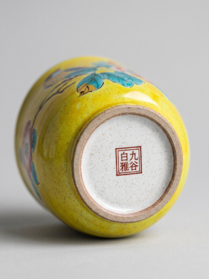 Yellow ceramic cup with floral design and Japanese stamp on a gray background