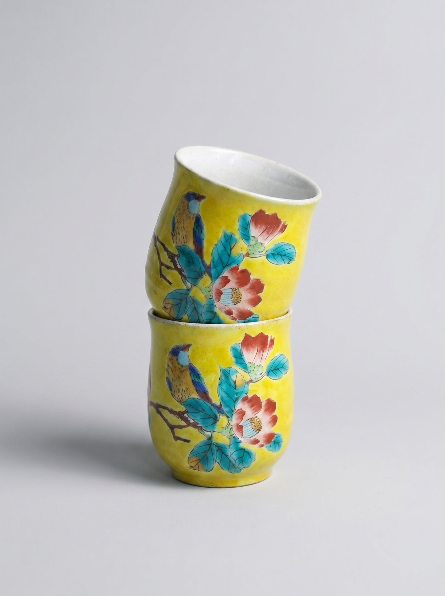 Two yellow ceramic cups with floral designs stacked on a light gray background