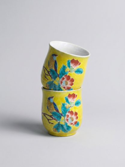 Two yellow ceramic cups with floral designs stacked on a light gray background