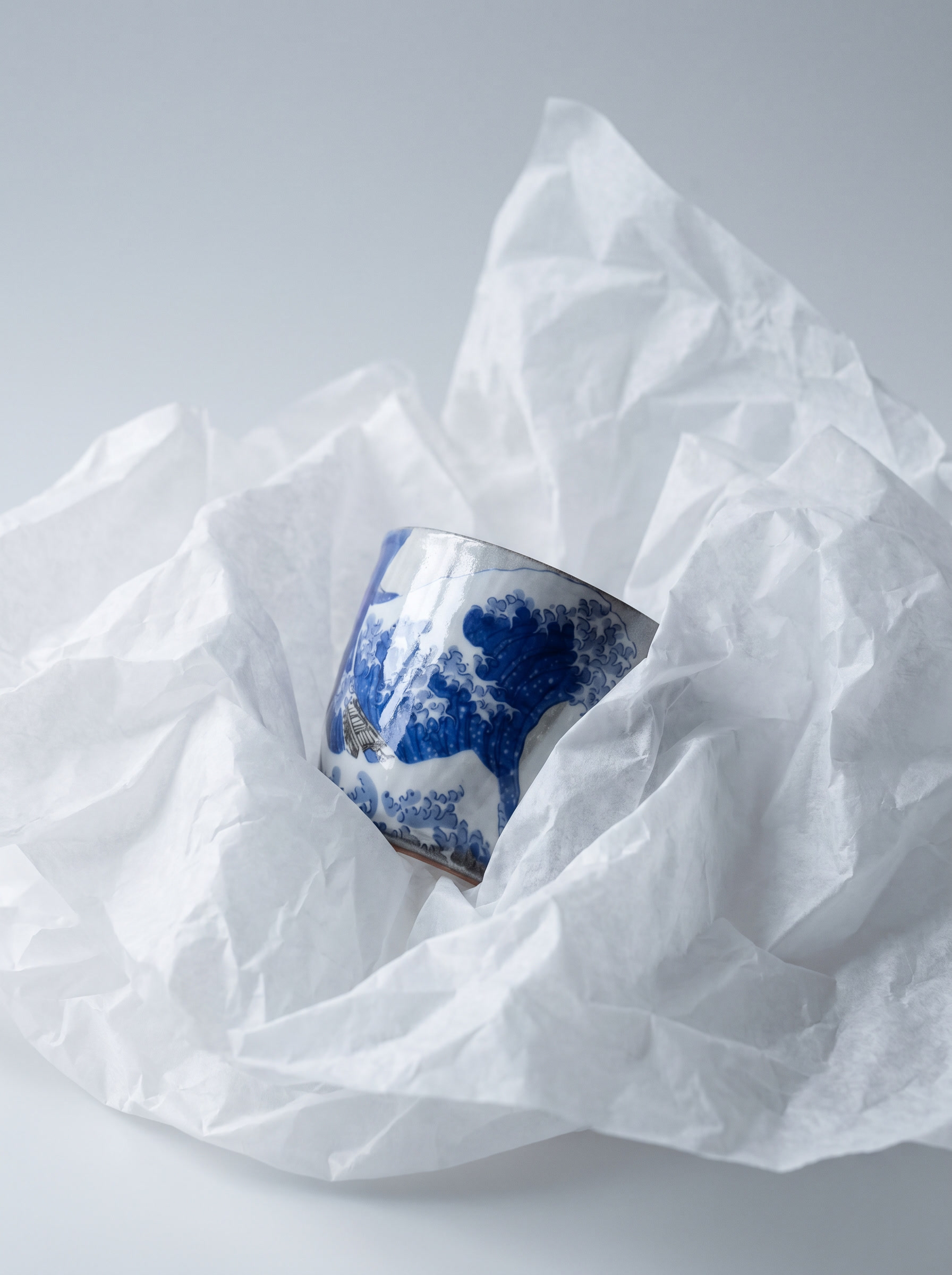 japanese ceramic teacup with wave of kanagawa design partially hidden by crumpled white paper on a light gray background