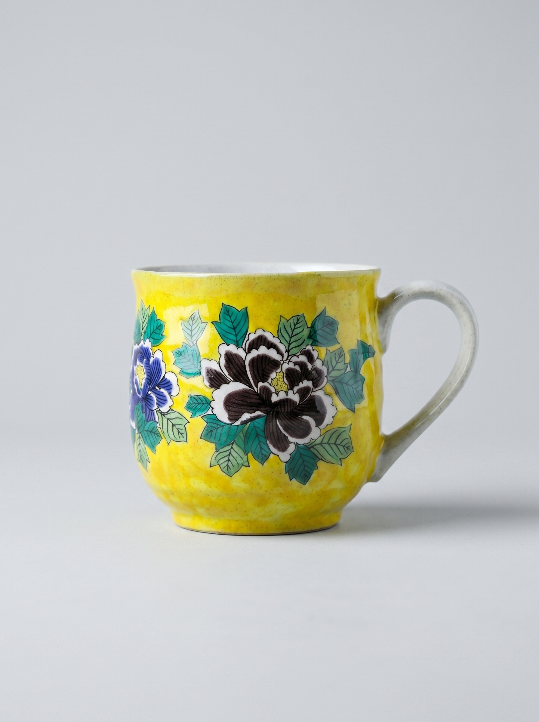 Yellow Japanese ceramic mug with floral design in yoshidaya style on a gray background