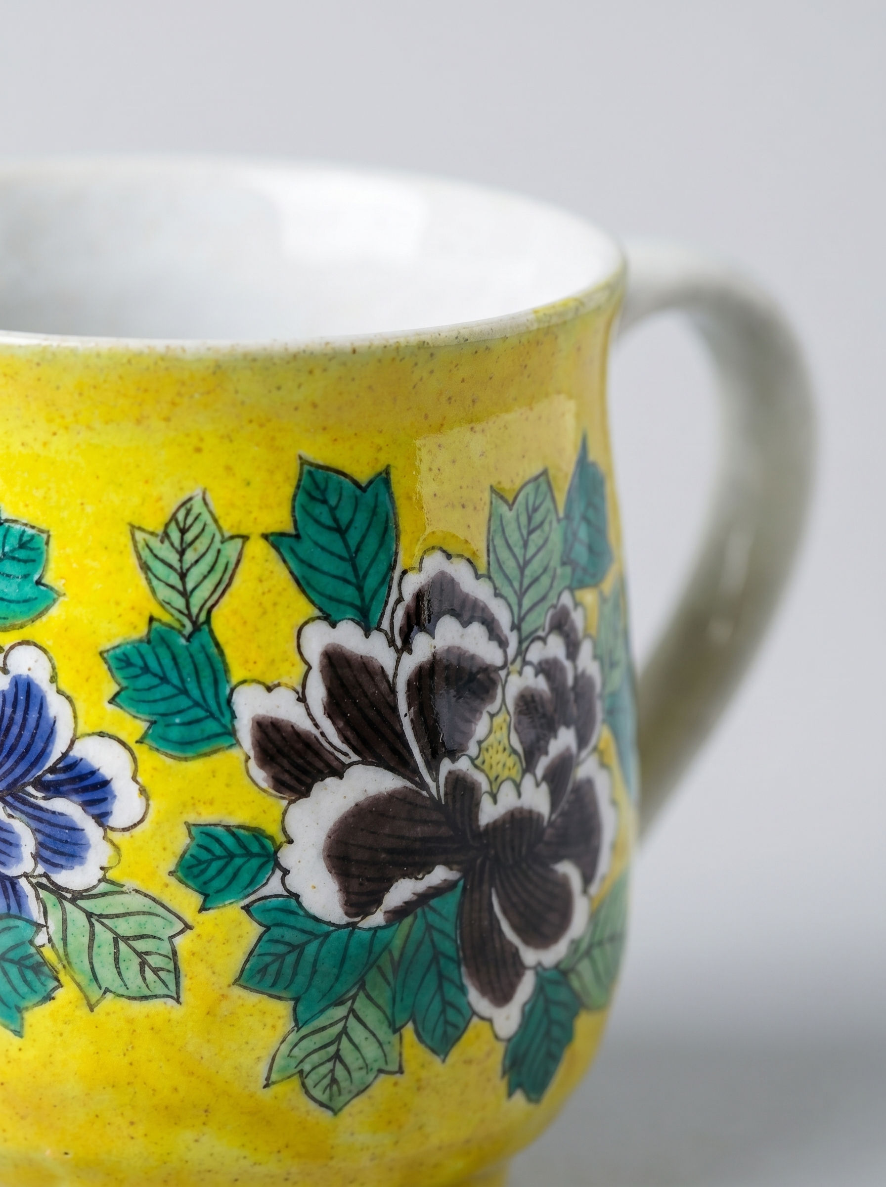 Close up of yellow ceramic mug with floral patterns on a white background