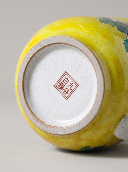 Close-up of a yellow ceramic cup with a visible brand logo on a gray background