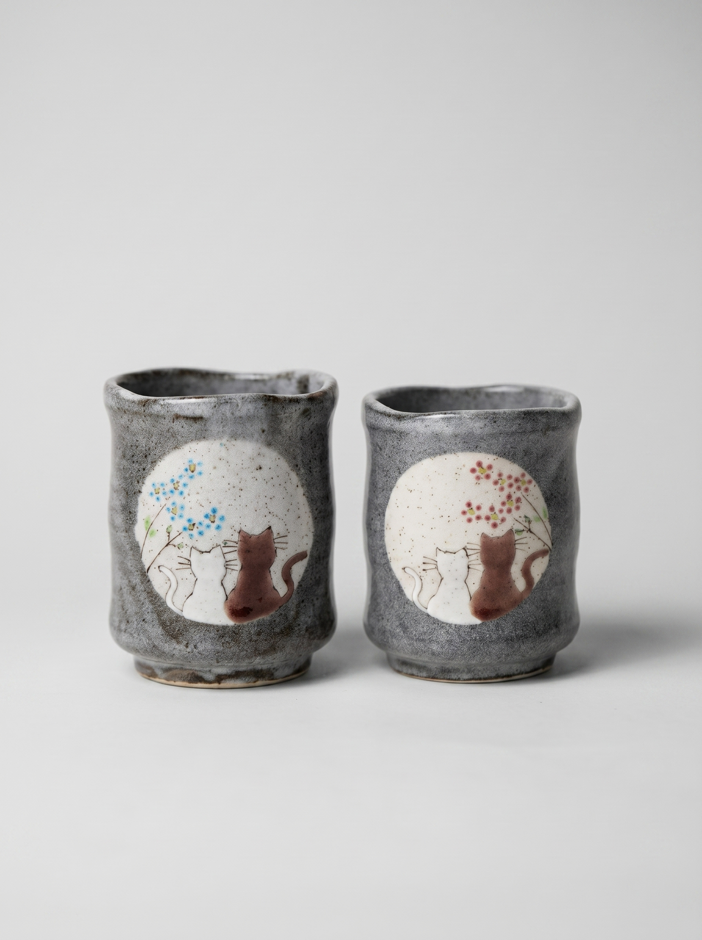 Set of two Japanese ceramic teacups with no handle with a cats in sunny spot yunomi design on a grey background