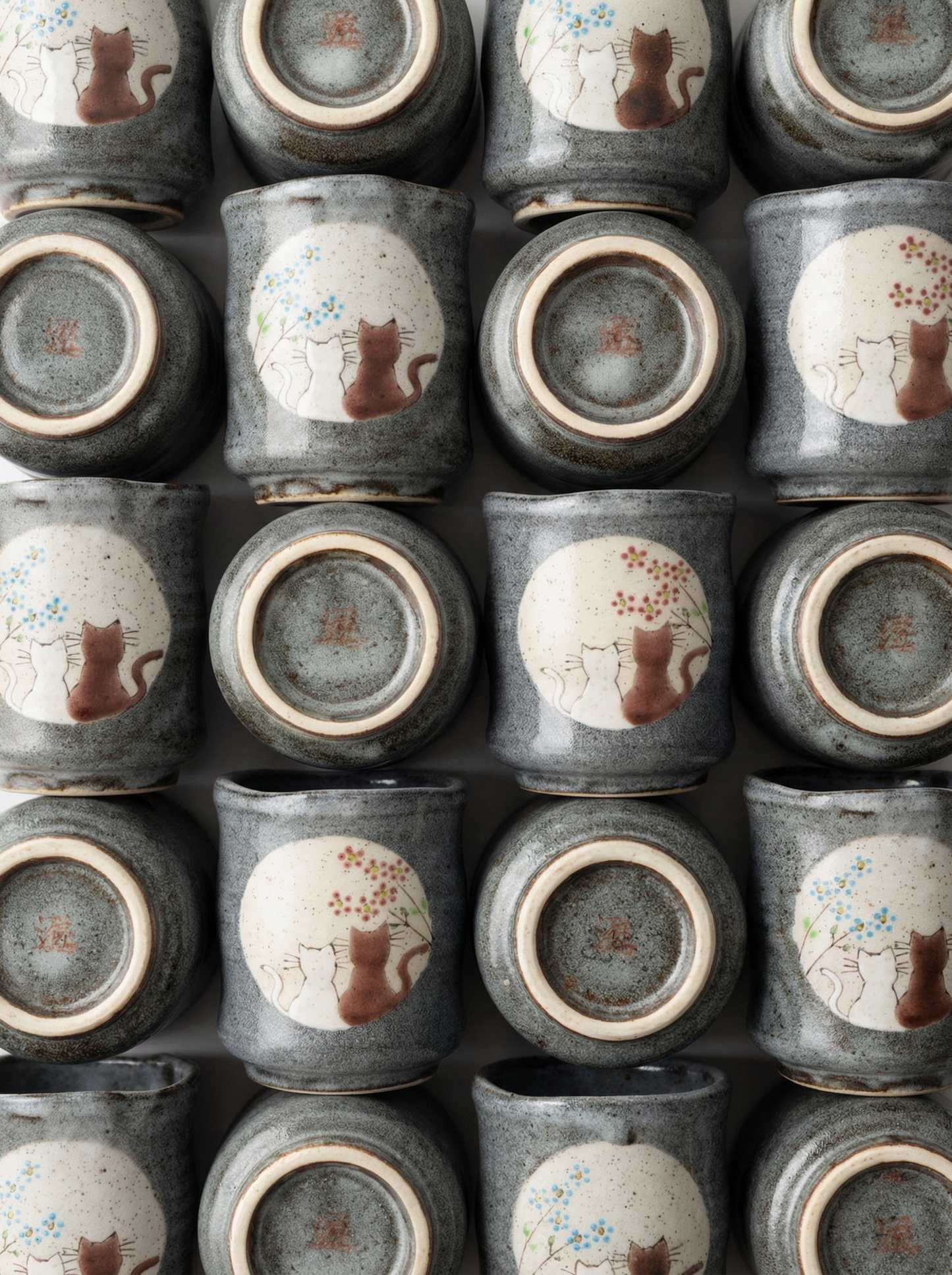 Multiple Japanese ceramic teacups with no handle with a cats in sunny spot yunomi design on a grey background