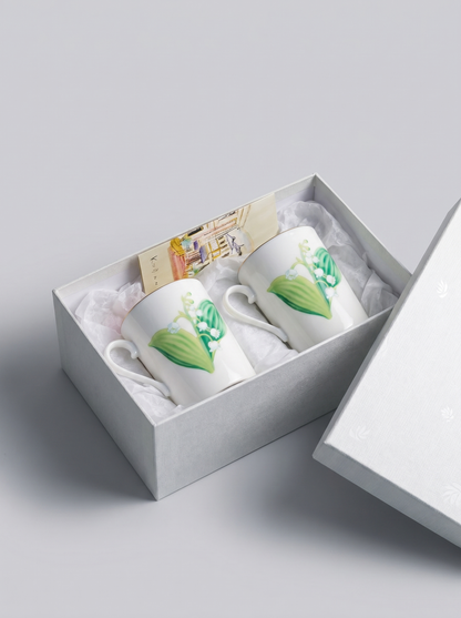 Two white porcelain teacups with lily of the valley designs in a gift box on a light gray background