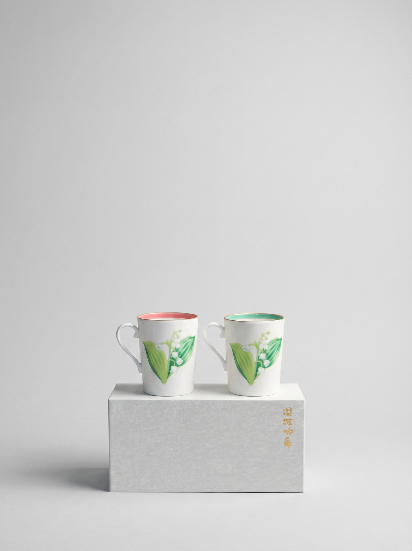Two ceramic teacups with floral design on a white gift box against a light gray background