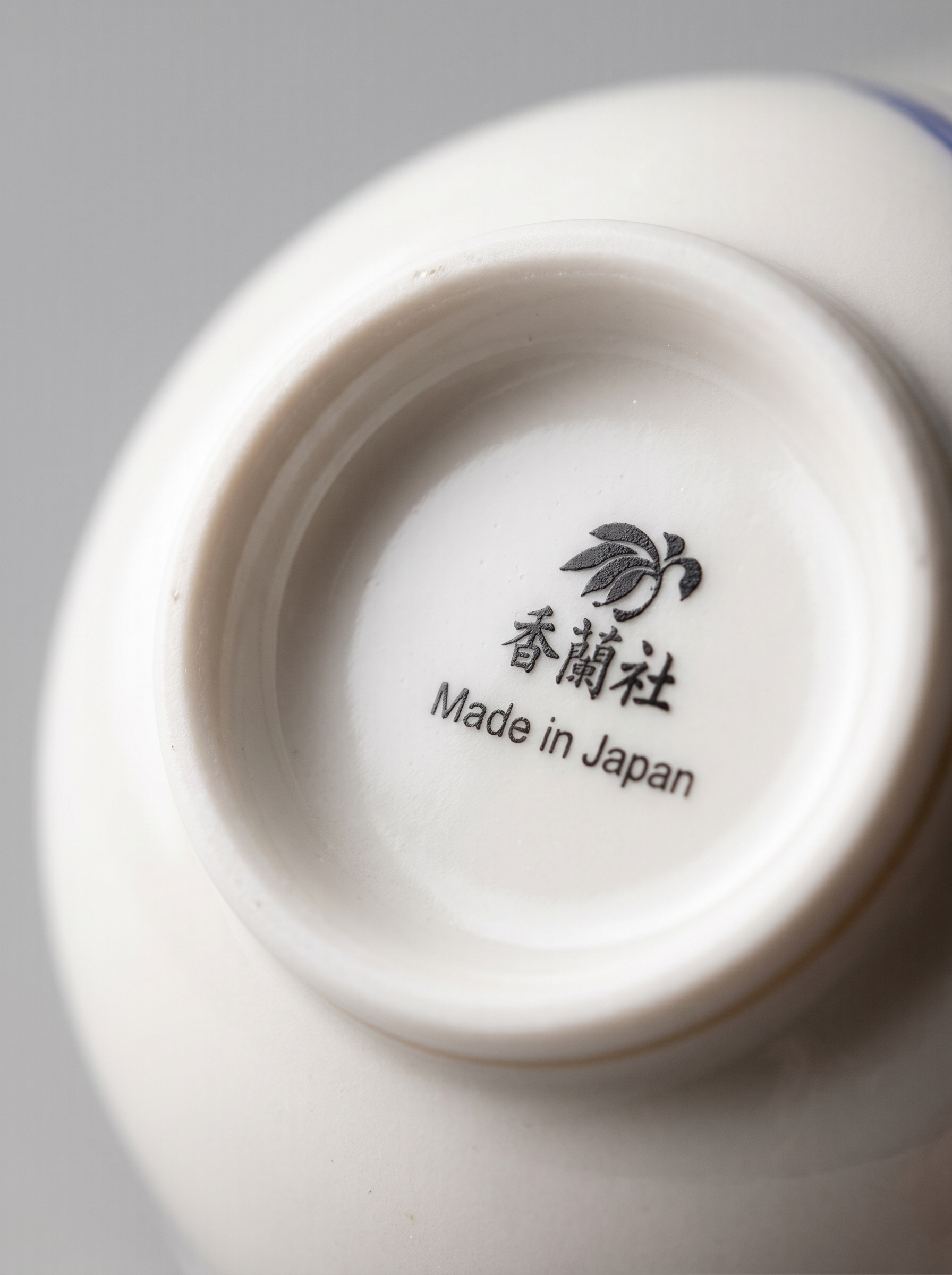 Close-up of a white porcelain teacup with 'Made in Japan' text on a gray background