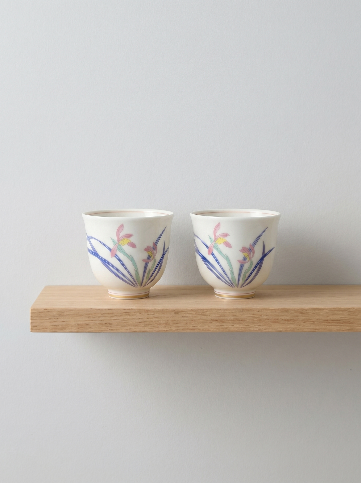 Two ceramic teacups with floral designs on a wooden shelf against a light gray background