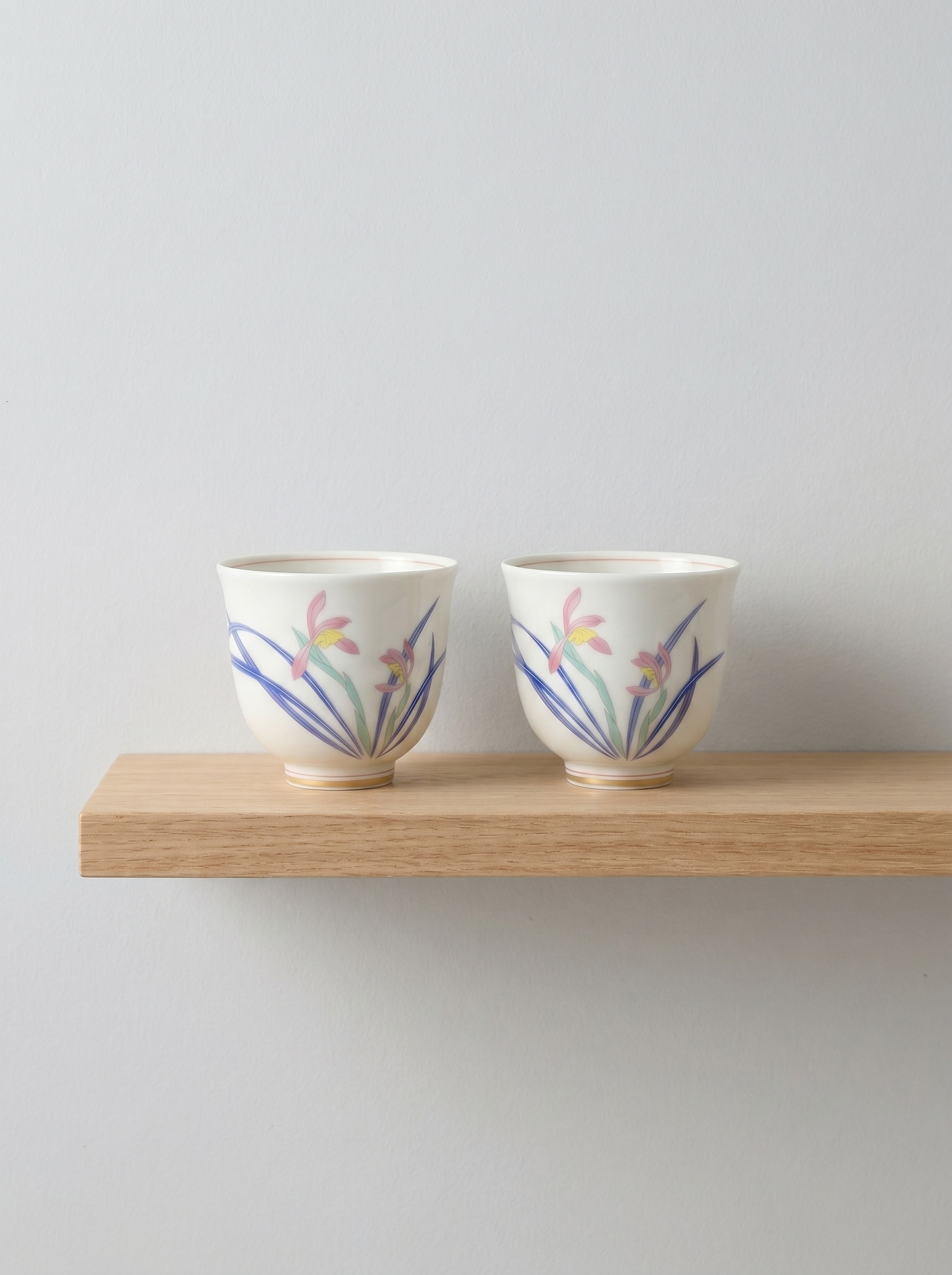 Two ceramic teacups with floral designs on a wooden shelf against a light gray background