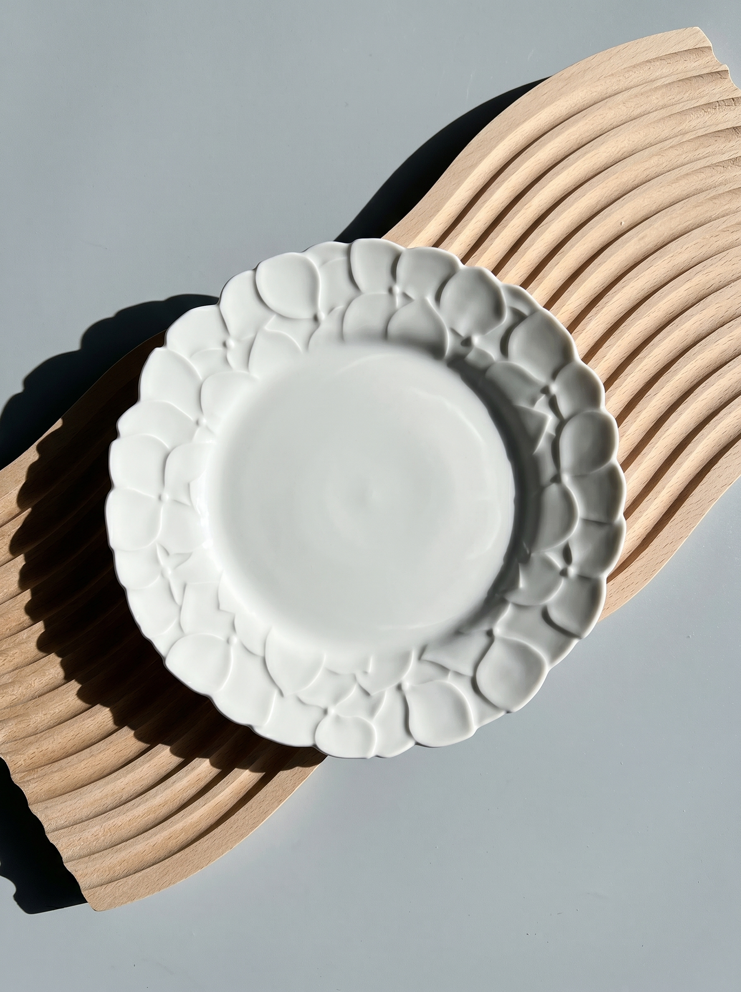 White Japanese koransha decorative plate with embossed surface on a light gray background, harsh light