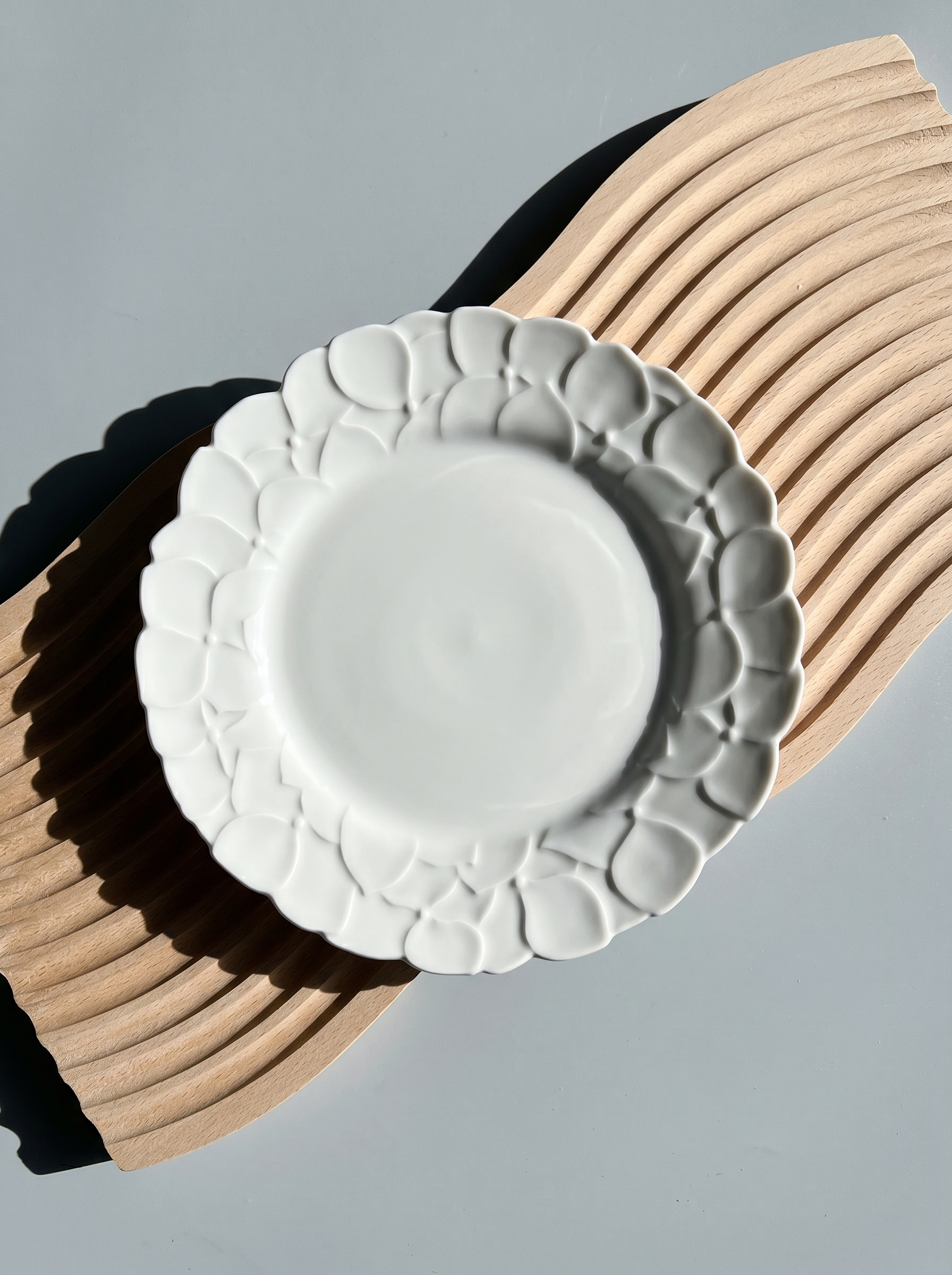 White Japanese koransha decorative plate with embossed surface on a light gray background, harsh light