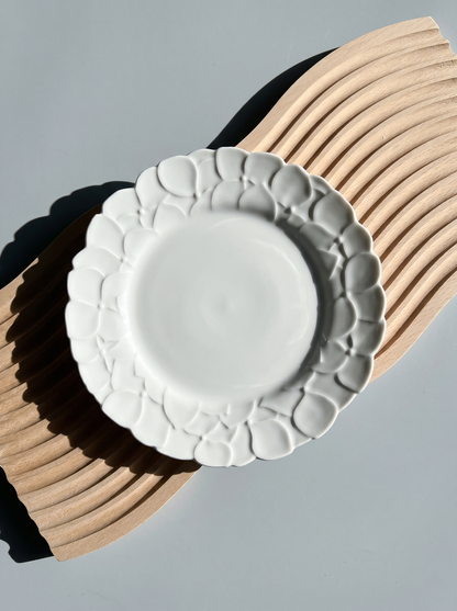 White Japanese koransha decorative plate with embossed surface on a light gray background, harsh light