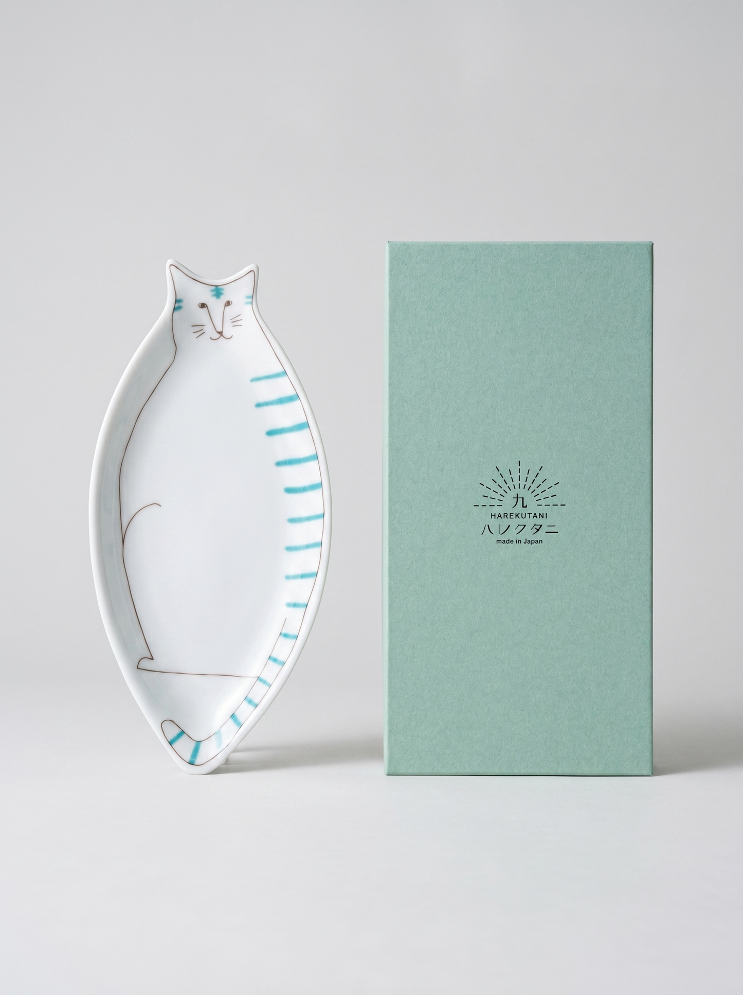 Cat-shaped ceramic dish next to a green box with a brand logo on a light gray background