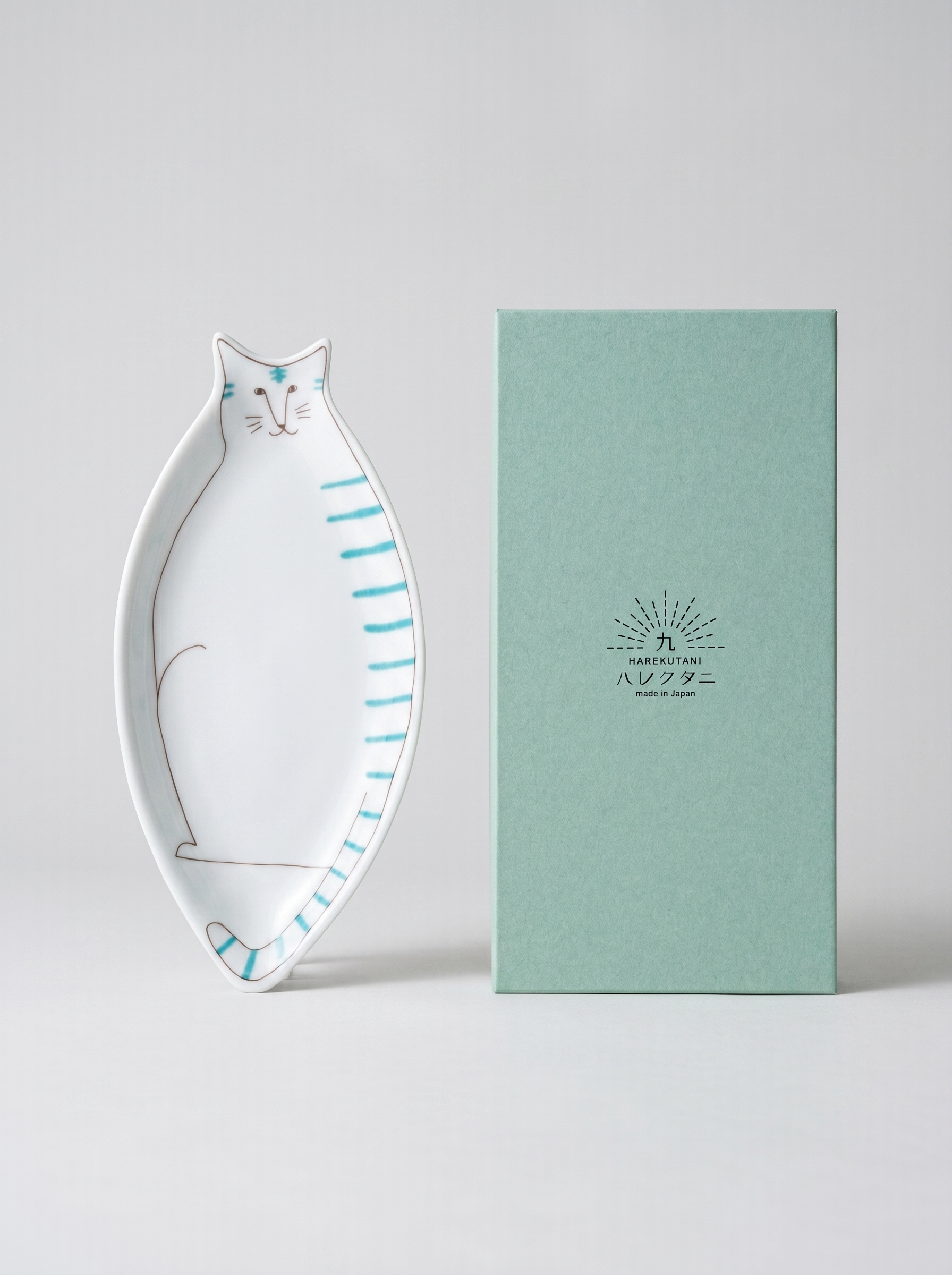 Cat-shaped ceramic dish next to a green box with a brand logo on a light gray background