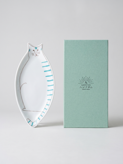 Cat-shaped ceramic dish next to a green box with a brand logo on a light gray background