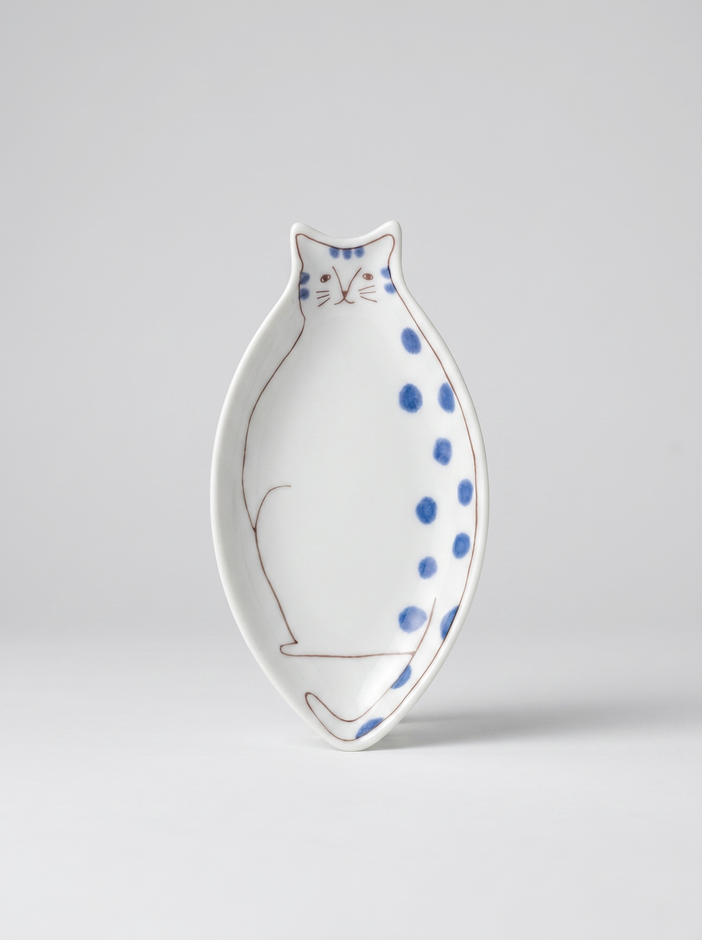 Japanese cat-shaped kutani ceramic sauce plate with blue polka dots on a light gray background