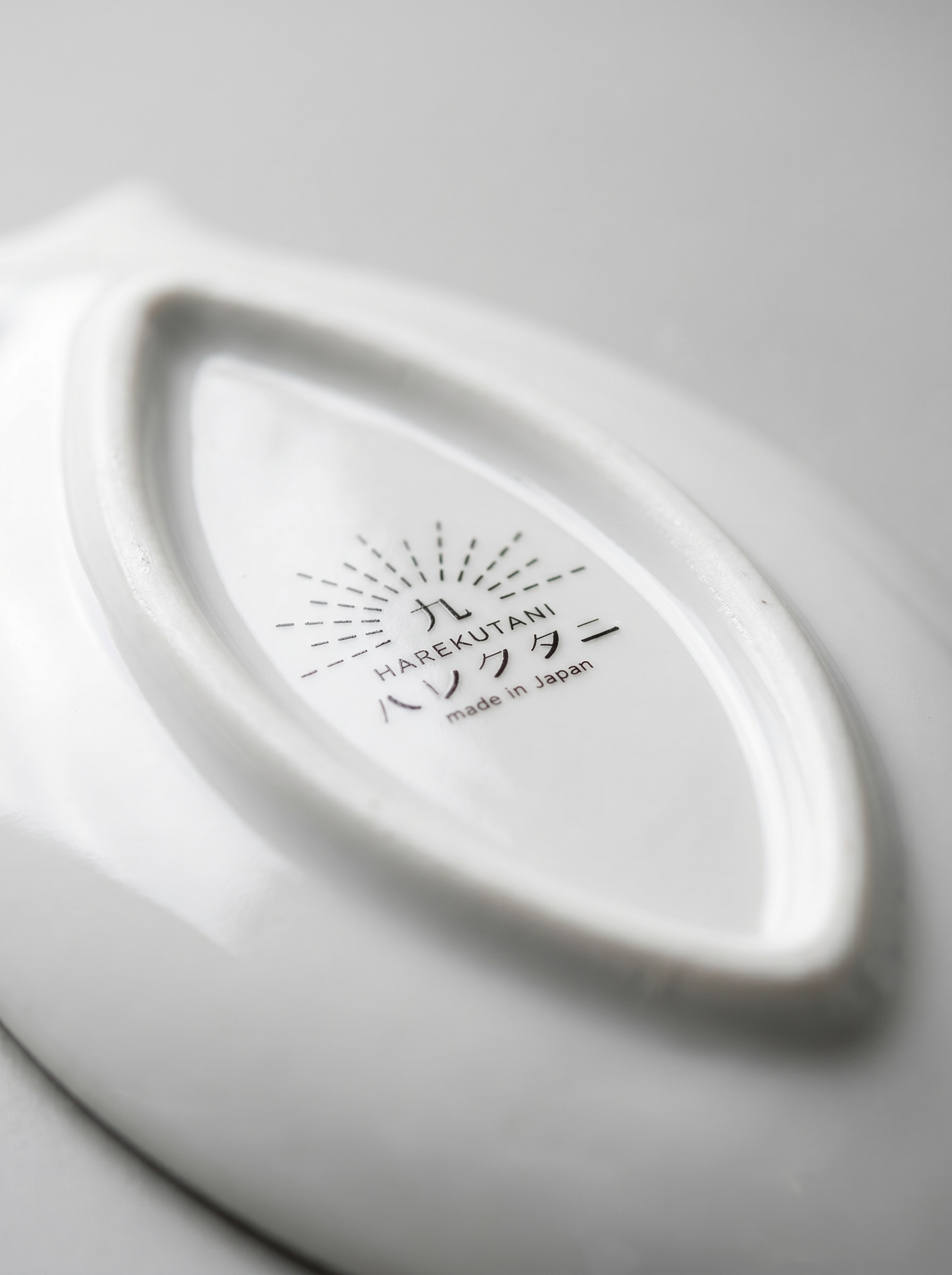 Close-up of a white ceramic product with 'Harekutani' branding on a light gray background