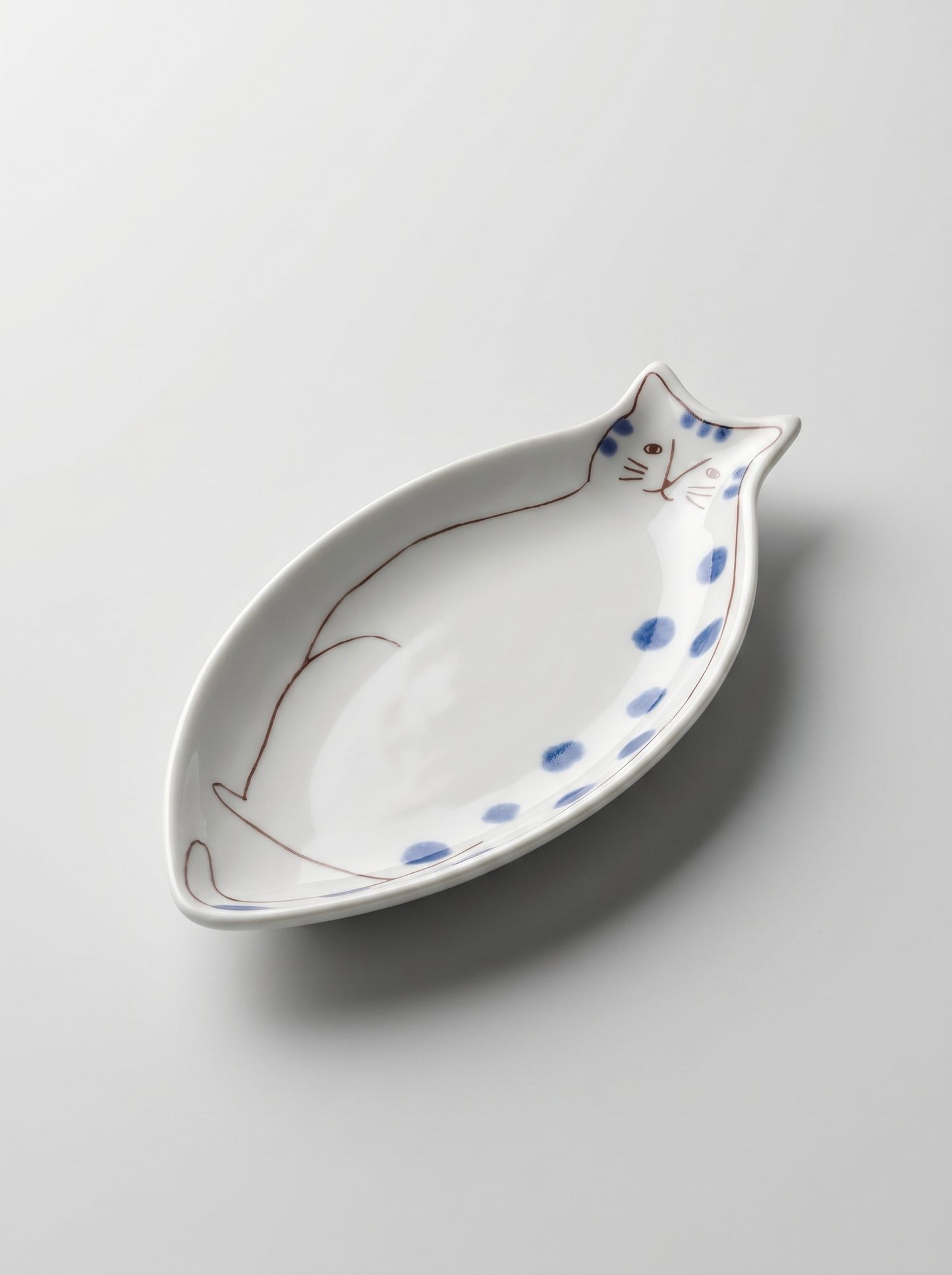 Cat-shaped ceramic dish with blue spots on a light gray background