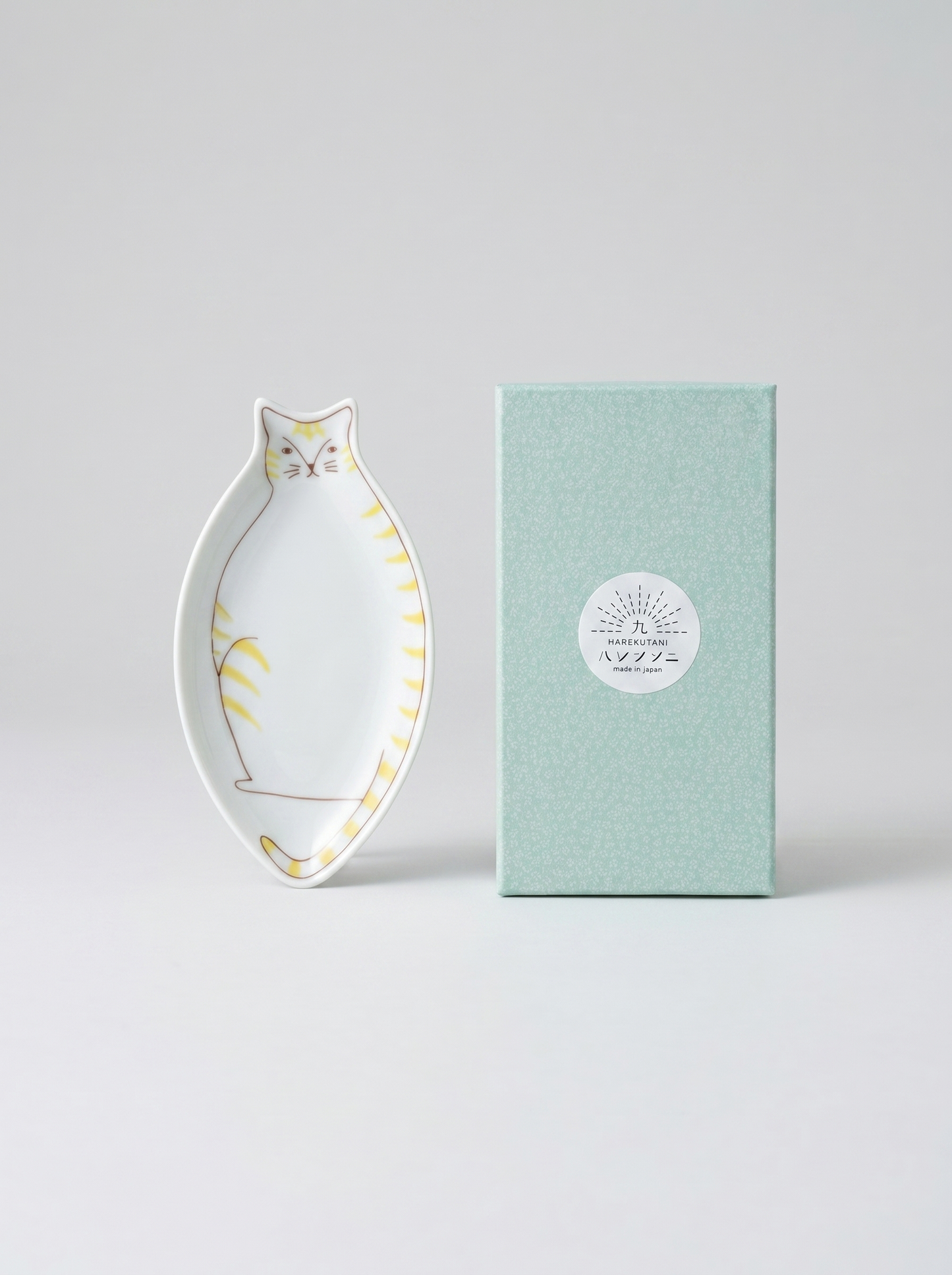 Decorative cat-shaped plate with yellow accents next to a green box on a light gray background