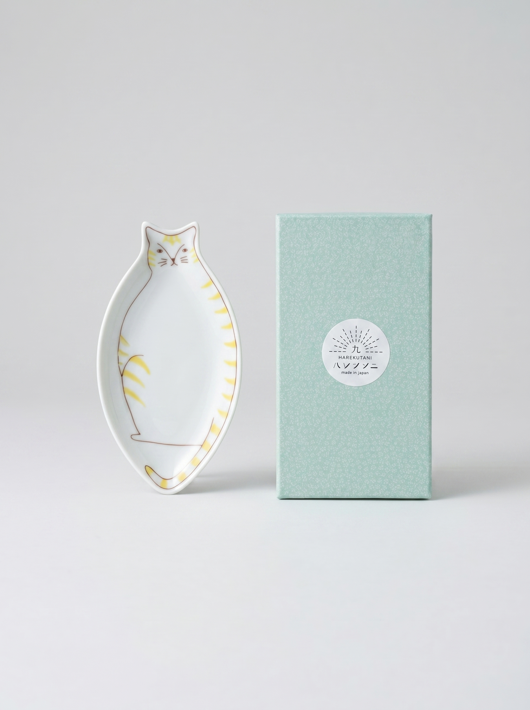 Decorative cat-shaped plate with yellow accents next to a green box on a light gray background