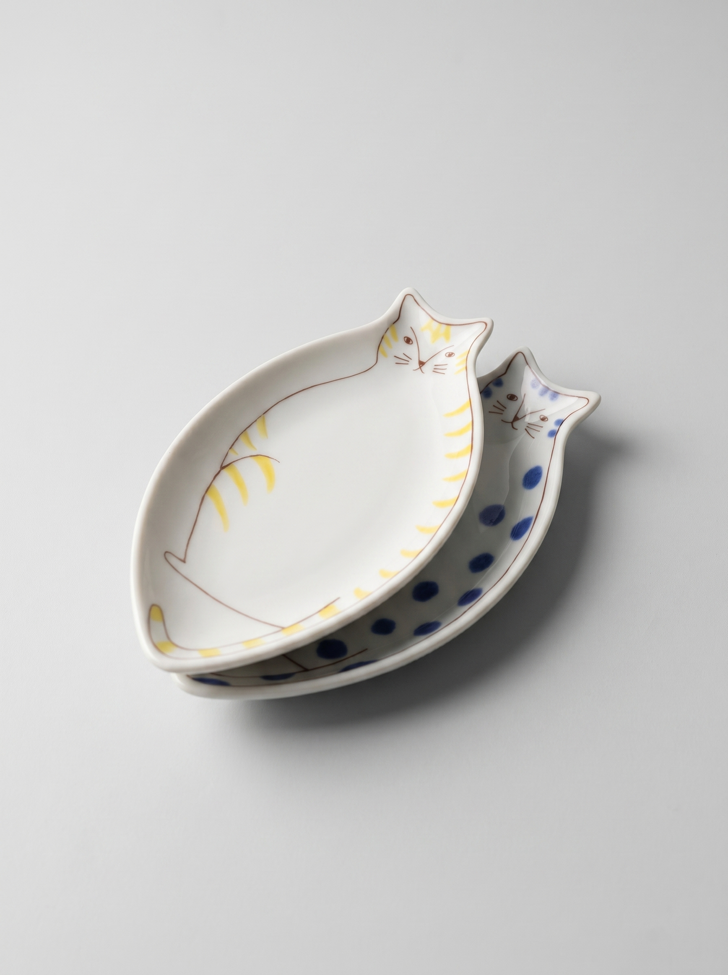 Cat-shaped ceramic dish with white body and blue polka dot tail on a light gray background