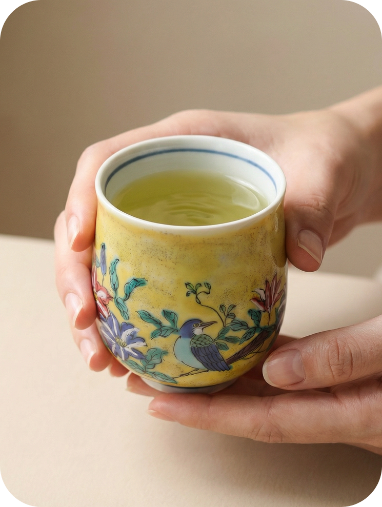 hands hold japanese ceramic teacup with a hand-painted design in yoshidaya style with birds on a branch