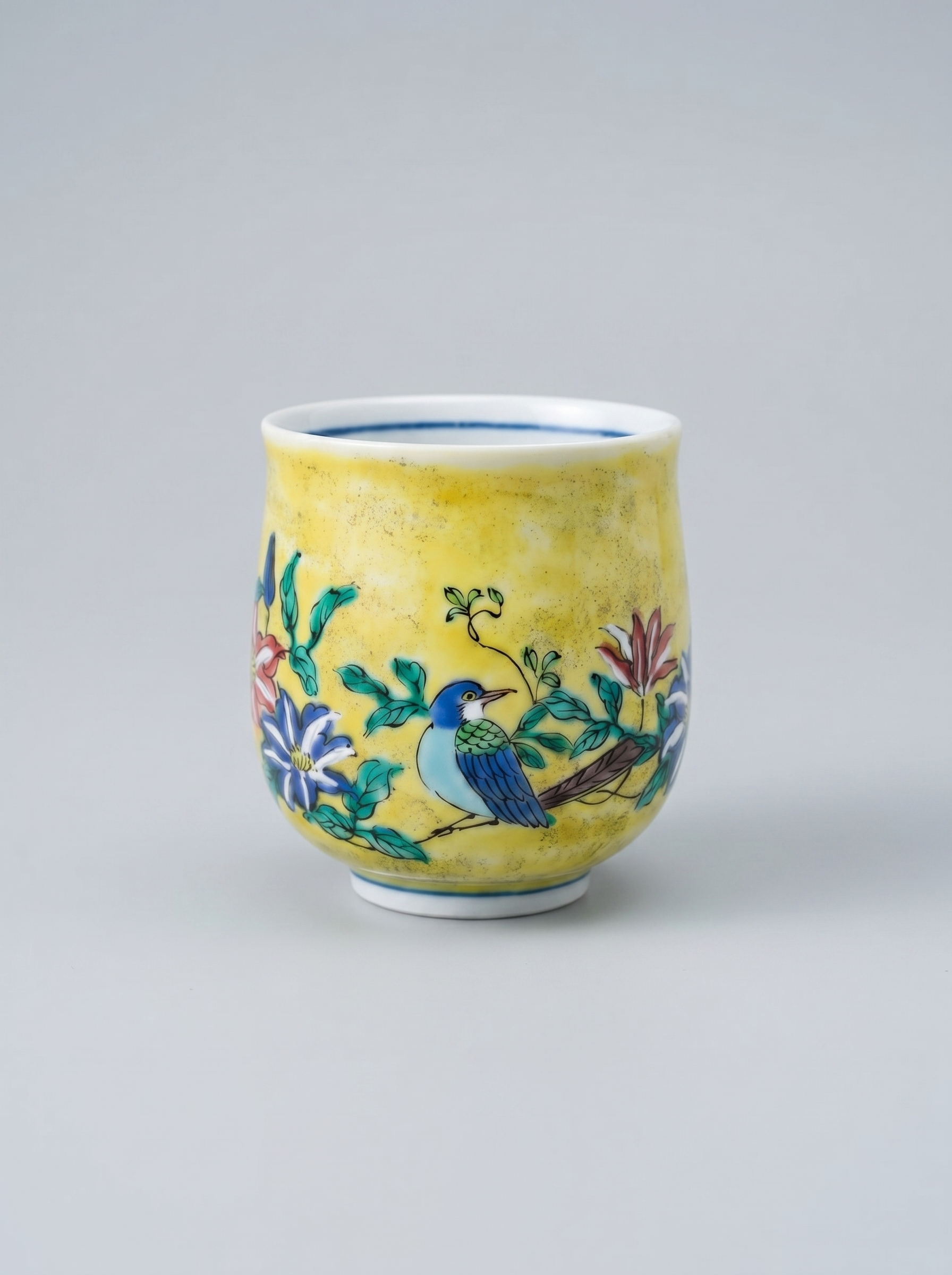 Japanese kutani yunomi ceramic cup with floral and bird design in yoshidaya style on a gray background