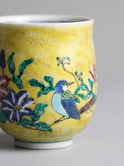 Close up of ceramic cup with floral and bird design on a yellow background