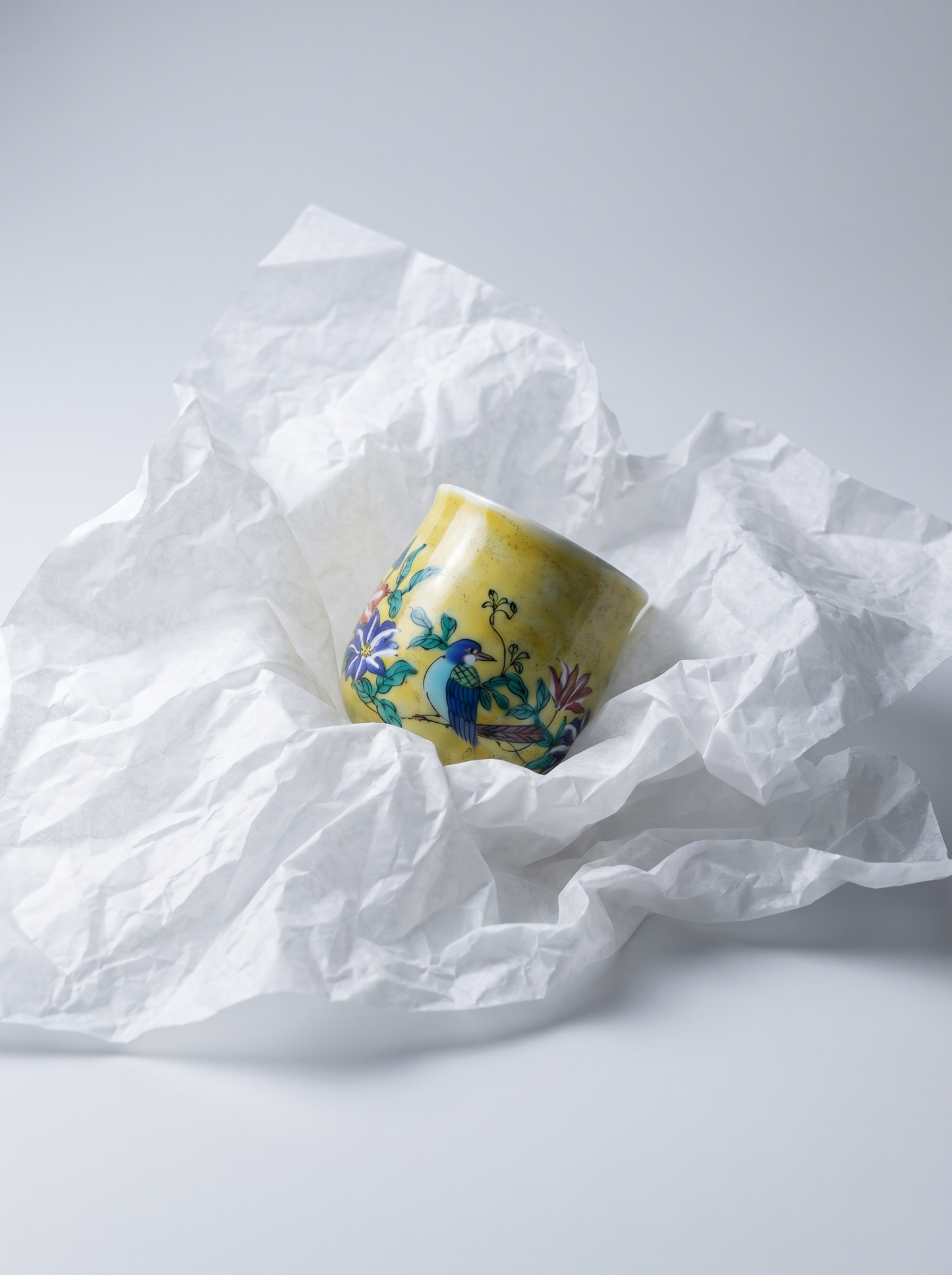 Decorative ceramic cup with floral design on crumpled white paper against a light gray background